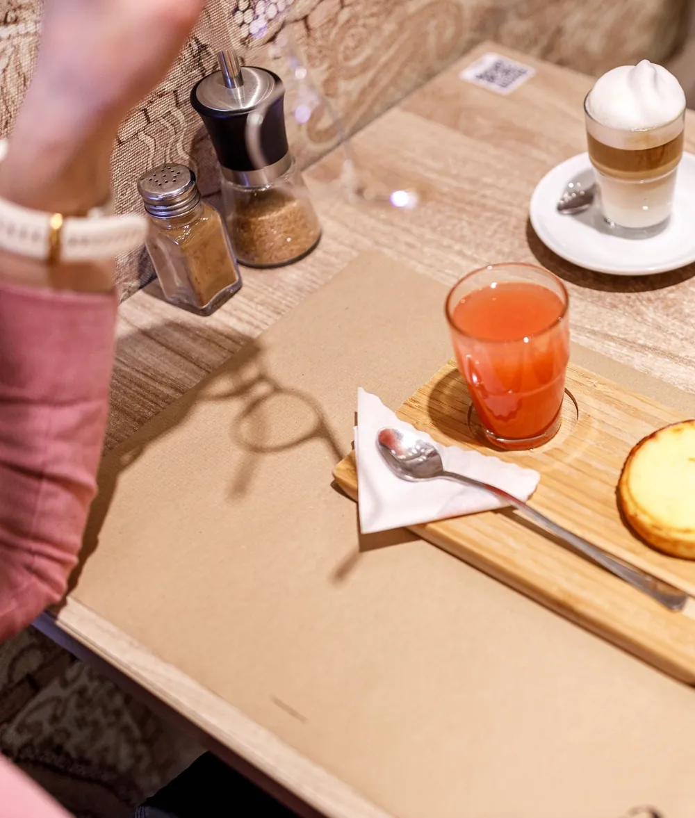 Latte macchiato, suc natural și cheesecake pe o masă Dolissima